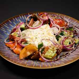 A beautifully presented plate of Greek salad featuring fresh tomatoes, cucumbers, red onions, and feta cheese, served on an ornate blue dish.