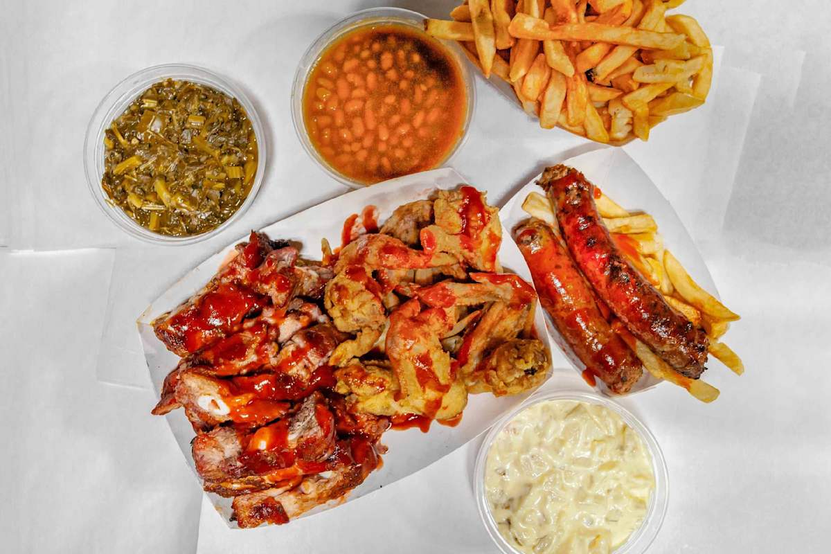 Assortment of BBQ foods including ribs, wings, sausage, fries, baked beans, and coleslaw.