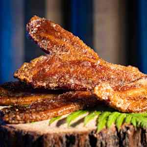 A close-up shot of crispy, golden-brown bacon strips on a wooden surface with a green leaf garnish.