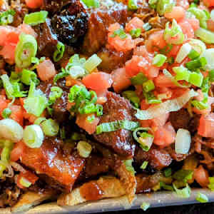 Close-up of BBQ dish with meat, diced tomatoes, and green onions.