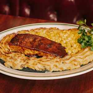A dish with a piece of meat on a bed of mashed potatoes and corn, garnished with parsley.