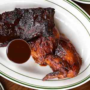 A plate of ribs and chicken with a side of BBQ sauce.
